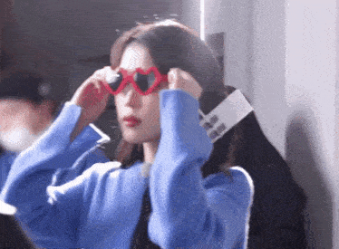 a woman in a blue sweater is wearing heart shaped sunglasses