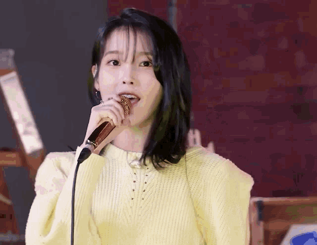 a woman is singing into a microphone while wearing a yellow sweater