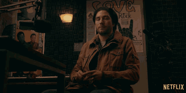 a man is sitting in front of a microphone in front of a love rock poster
