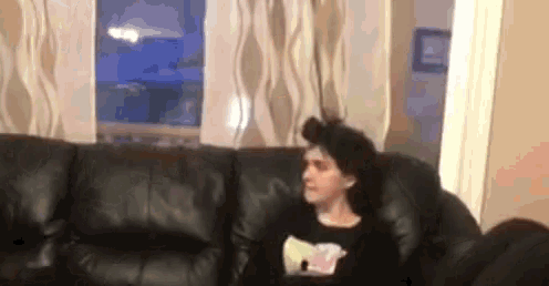 a woman is sitting on a couch in a living room holding a bag of popcorn .