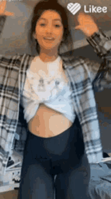 a woman wearing a plaid shirt and black leggings is dancing in a room .