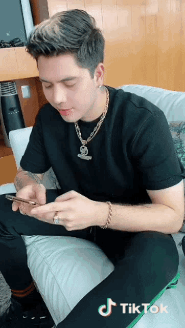 a man is sitting on a couch looking at his phone with a tiktok sticker on the bottom