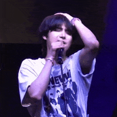 a young man is singing into a microphone while wearing a t-shirt that says new