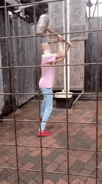 a woman in a pink shirt is standing in a cage holding a ruler .