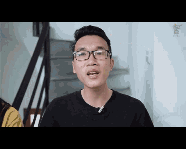 a man wearing glasses and a black shirt stands in front of a staircase