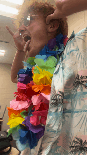 a man wearing a hawaiian shirt and a lei around his neck is sticking his tongue out