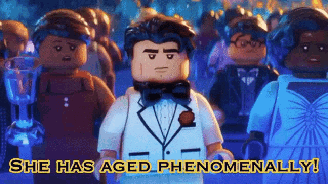 a lego man in a tuxedo stands in front of a crowd with the words she has aged phenomenally above him