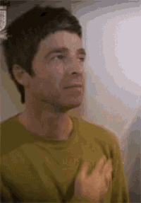 a man in a yellow shirt is standing in front of a wall with his hand on his chest .