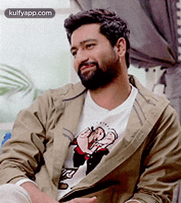 a man with a beard is wearing a jacket and a t-shirt with a cartoon character on it .