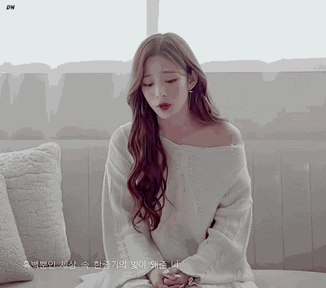 a woman wearing a white sweater sits on a couch