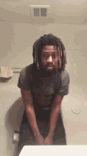 a man with dreadlocks stands in front of a bathroom sink