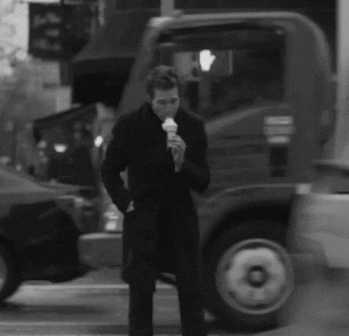 a man in a black coat eating an ice cream cone