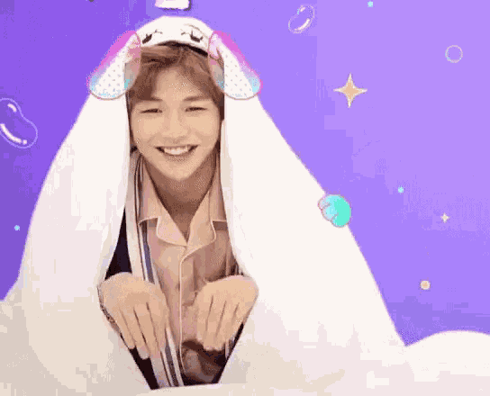 a young man wearing bunny ears is looking out of a hole in a white blanket .