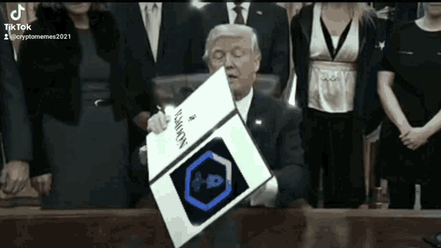 a man in a suit is sitting at a table holding a sign that says ' xbox ' on it