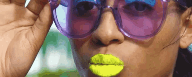 a close up of a woman wearing sunglasses and neon yellow lipstick .