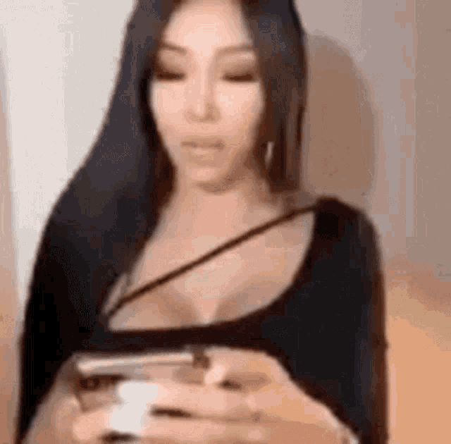 a woman with long black hair is holding a cell phone in her hand .