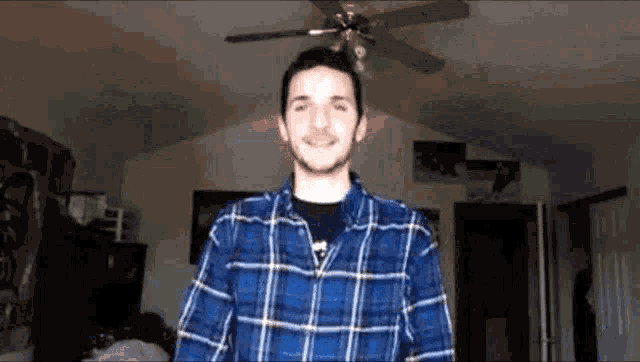 a man in a plaid shirt is standing in front of a ceiling fan .