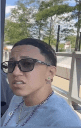 a man wearing sunglasses and a necklace is making a face .