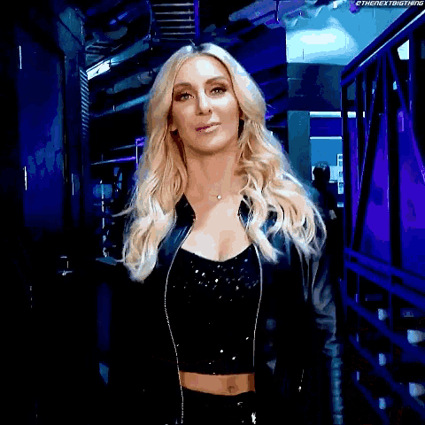 a woman in a black jacket and crop top is standing in a dark room .