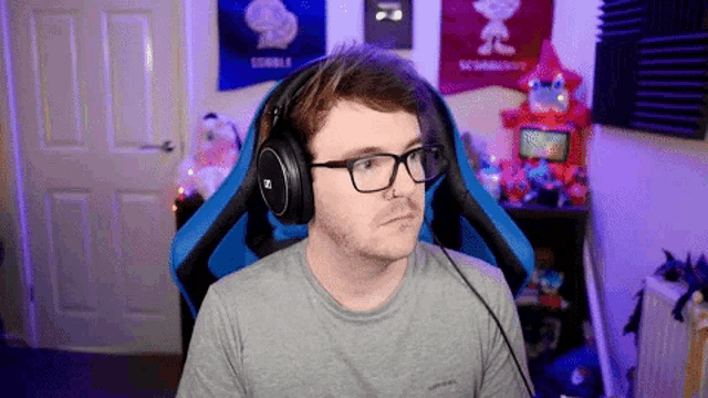 a man wearing glasses and headphones is sitting in a blue gaming chair .