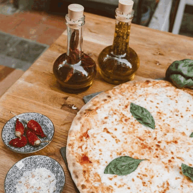 a pizza sitting on a wooden table next to bottles of oil