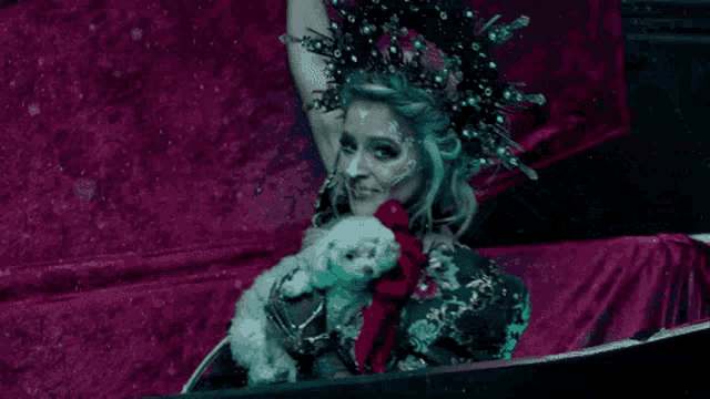 a woman with a crown on her head is holding a small white dog in her arms .