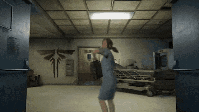 a woman in a blue dress is standing in a room with a hospital bed on the wall