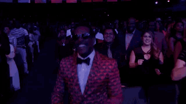a man in a red suit and bow tie is dancing in front of a crowd at a concert .