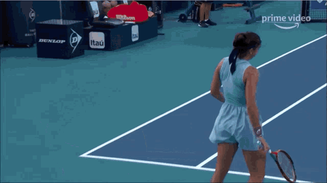a woman is holding a tennis racquet on a court sponsored by itaú