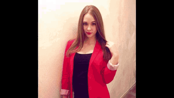 a woman wearing a red jacket and a black dress is standing next to a wall
