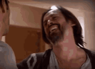 a man with long hair and a beard is laughing with another man .