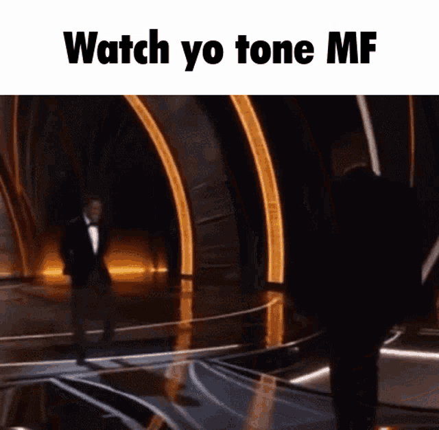 a man in a tuxedo stands on a stage with the words " watch yo tone mf " above him