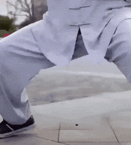 a person is standing on a sidewalk with their legs crossed and their hands in their pockets .