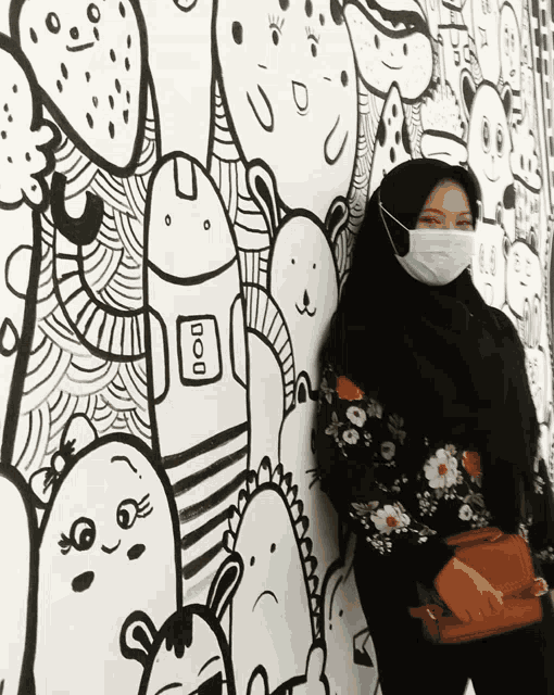 a woman wearing a face mask is standing in front of a wall with drawings on it and the word boo on it