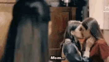 a couple of women are kissing in a kitchen while a ghost is standing behind them .