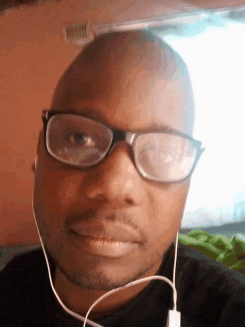 a bald man wearing glasses and ear buds looks at the camera