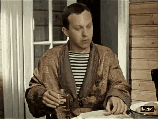 a man in a robe is sitting at a table with a bottle of alcohol in his hand .