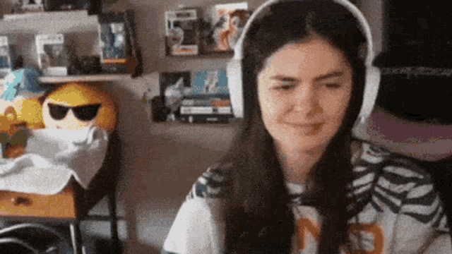 a woman wearing headphones is smiling in front of a shelf with a smiley face on it .