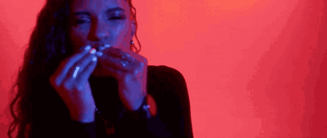 a woman is smoking a cigarette in a dark room with a red background .