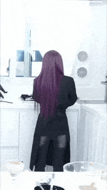 a woman with purple hair is standing in a white kitchen