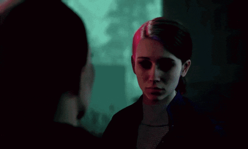 two women are looking at each other in a dark room with purple and green lights