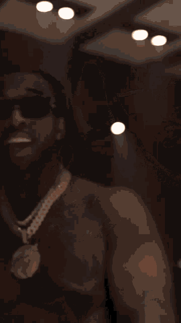 a man without a shirt is wearing sunglasses and a gold chain around his neck