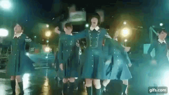 a group of girls in blue dresses are dancing in the rain in front of a bus .