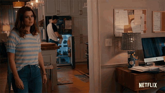 a woman in a striped shirt stands in a room with a netflix logo on the corner