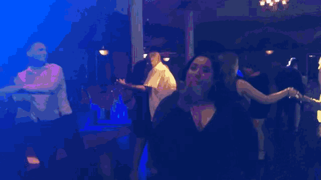 a woman in a black dress is dancing in a dark room with other people