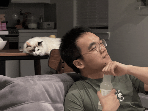 a man sitting on a couch with a cat laying on his head