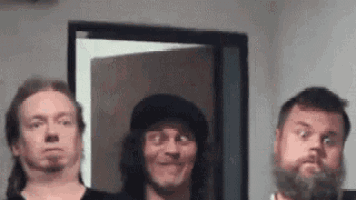 three men with beards are standing next to each other in a room making funny faces .