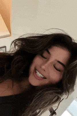 a woman with long dark hair is smiling with her eyes closed and her hair blowing in the wind .