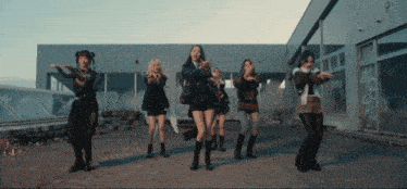 a group of women are dancing in front of a building with graffiti on it