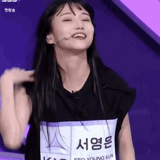 a woman wearing a black shirt and a name tag is smiling and holding her hair .